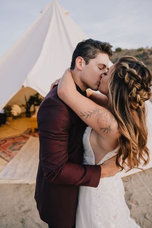 Bride and groom sharing romantic kiss in front of white boho bell tent at outdoor wedding.