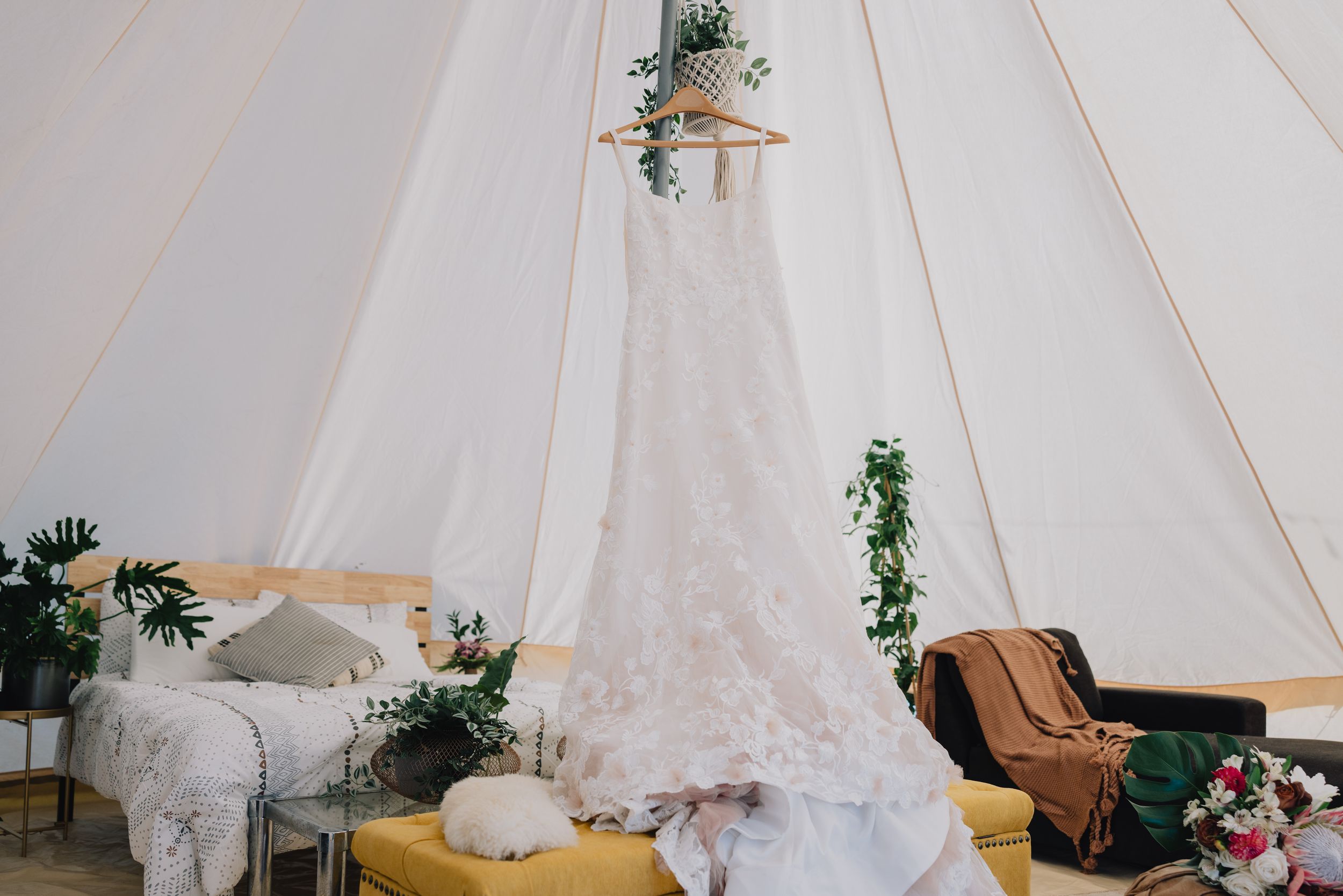 Wedding dress hanging in a boho bell tent with lush greenery and cozy furnishings.