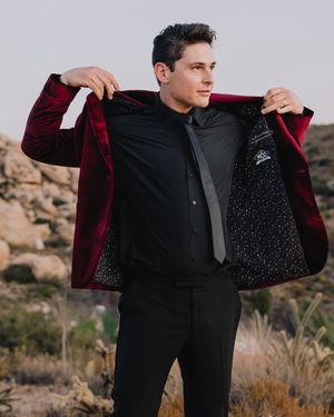 Groom reveals star-patterned lining of burgundy velvet blazer outdoors in rocky desert landscape.