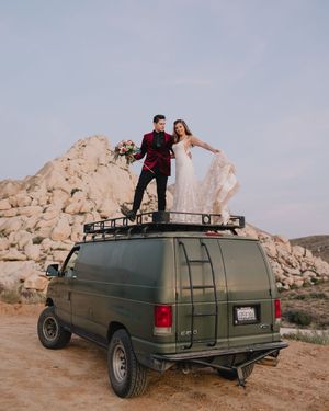 Wedding couple stands atop vintage green Ford van roof rack amid rocky desert landscape at dusk.