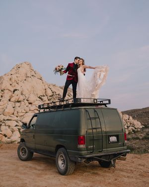 Bride and groom stand atop a green van in a desert landscape, sharing a romantic moment with rocky formations behind them.
