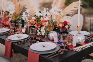 Elegant boho wedding tablescape with pampas grass, colorful florals, and jewel-toned glassware.