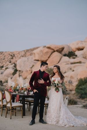 Elegant couple poses beside decorated desert wedding reception table with pampas grass and boulder backdrop.