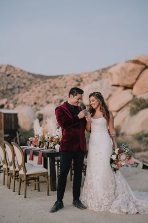 Smiling bride and groom toast with glasses beside elegant desert reception table at golden hour in Joshua Tree.