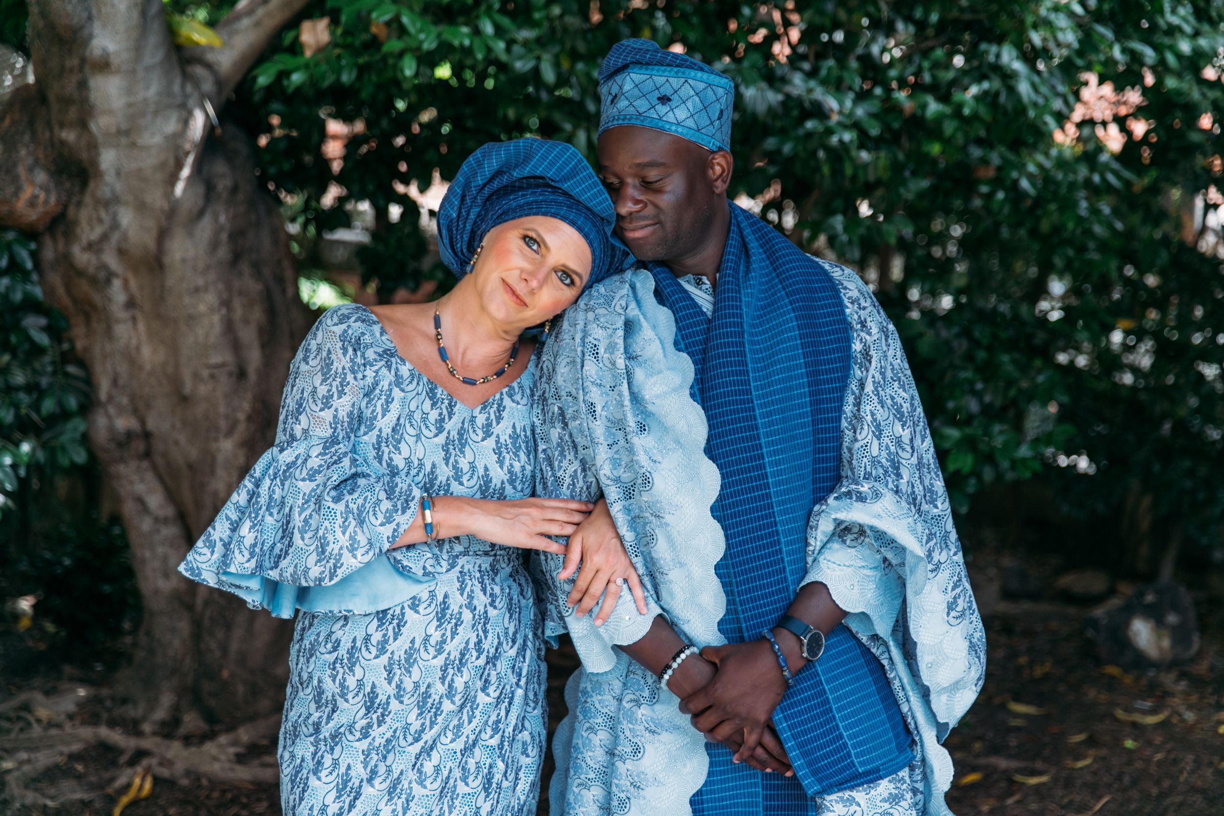 A couple shares a tender moment in an outdoor garden setting wearing blue coordinated outfits.