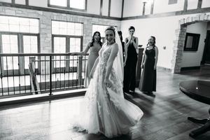Black and white photo of a wedding party walking through a bright indoor hallway with large windows.