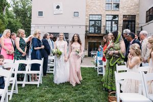 Wedding guests mingle and socialize during an outdoor reception at a stone venue on a sunny afternoon.