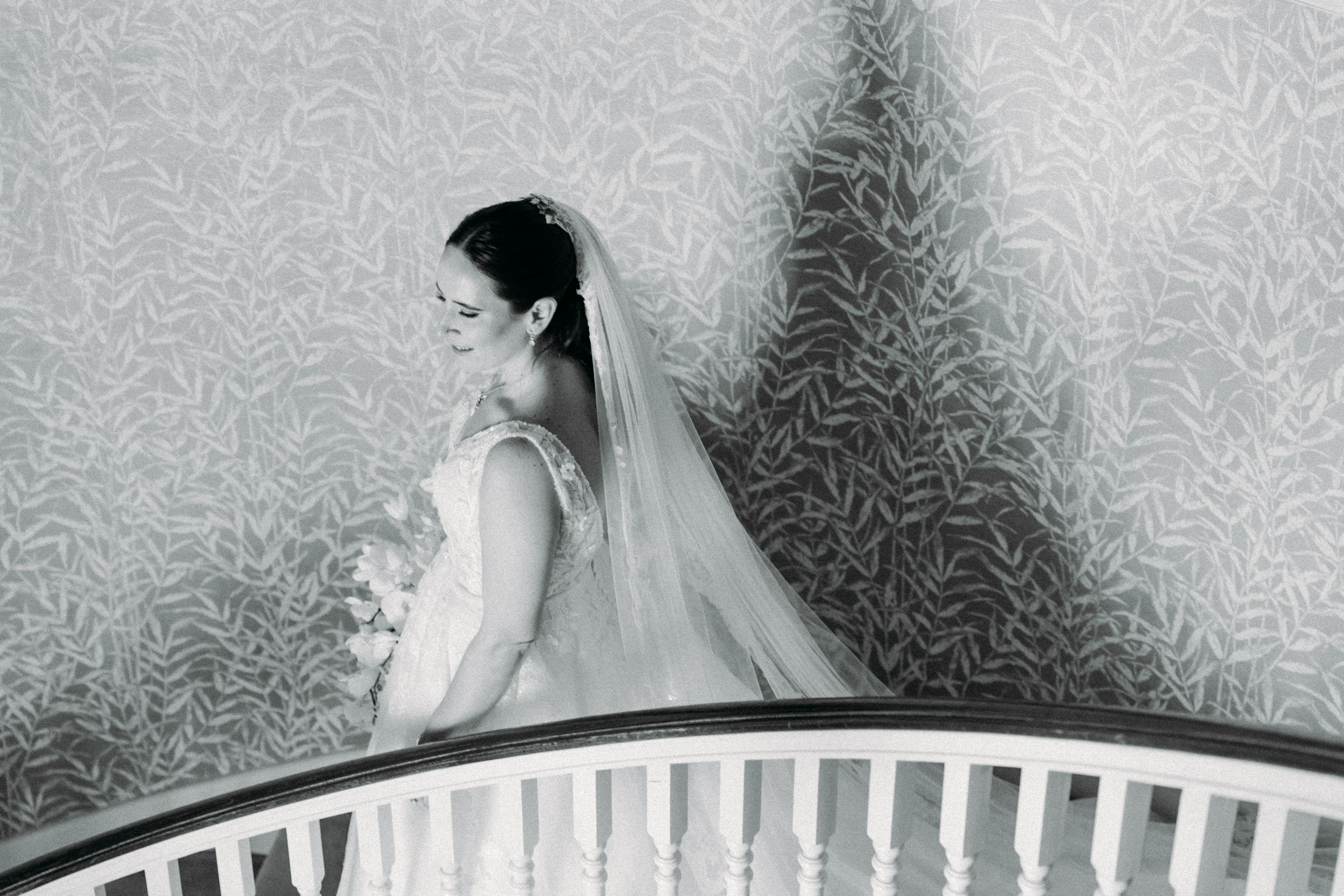 A sequence of black and white wedding photos showing details of a bride's veil and dress against a patterned wallpaper background.