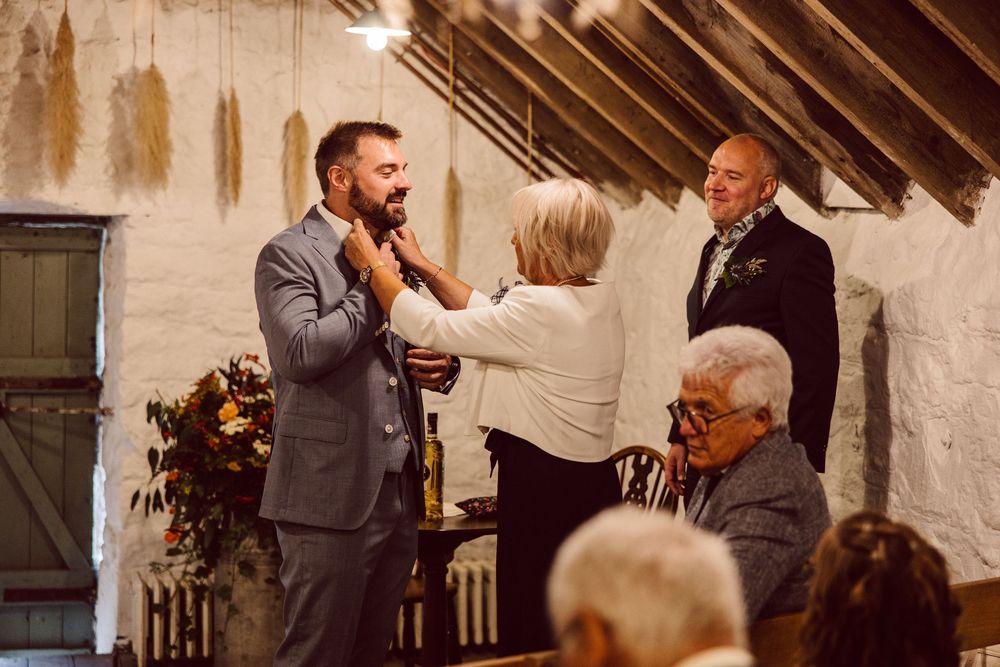 A group of people gather in a rustic room with exposed wooden beams during what appears to be a social event.