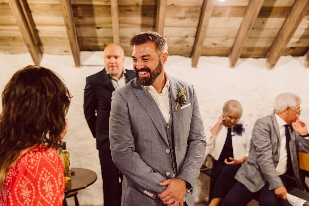 Wedding party in gray suits and a red dress gather for a candid celebration moment at an indoor venue.