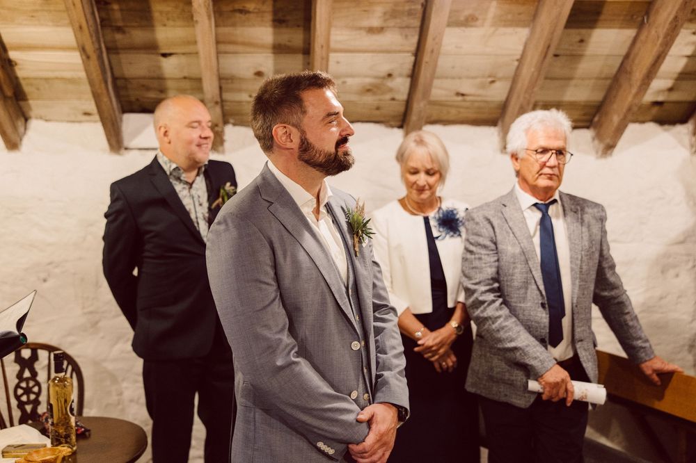 A group of formally dressed guests laugh and socialize during a wedding reception in a rustic wooden venue.