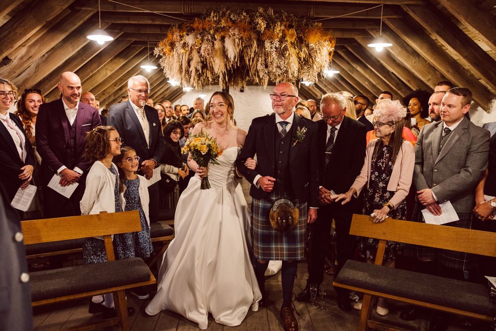 Wedding guests seated in wooden church pews celebrate joyfully during a ceremony in a warmly lit chapel.
