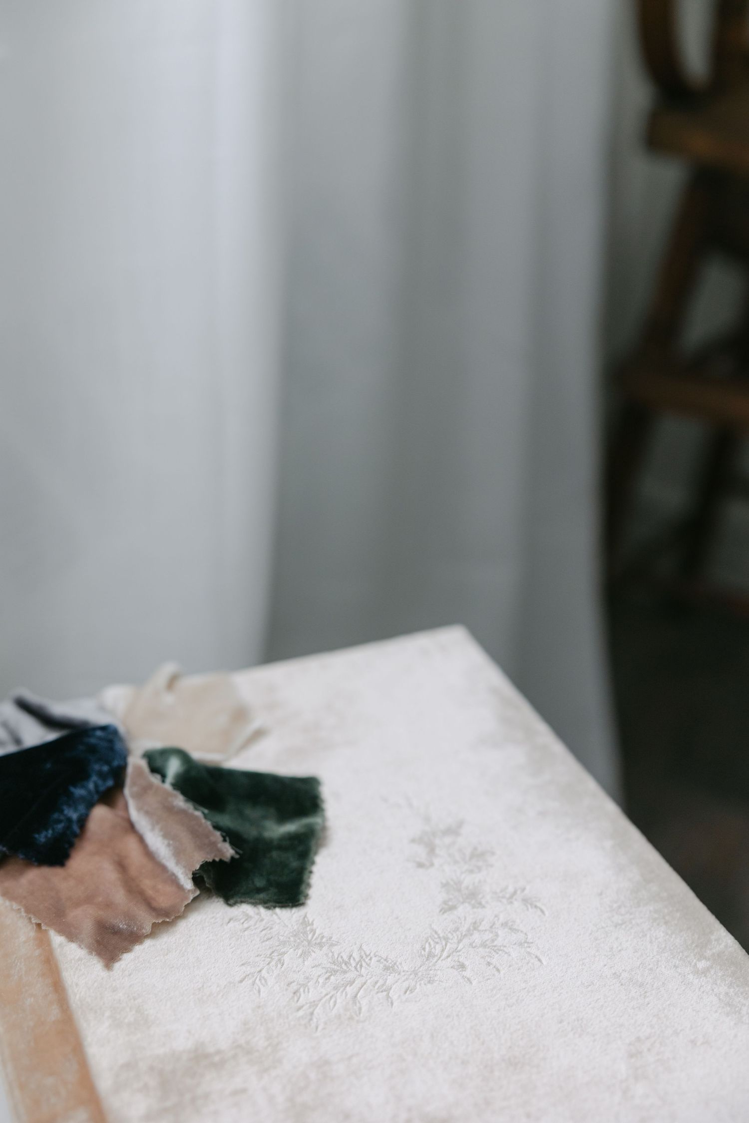 A close-up view of a green velvet bow resting on white lace fabric with delicate embroidered details.