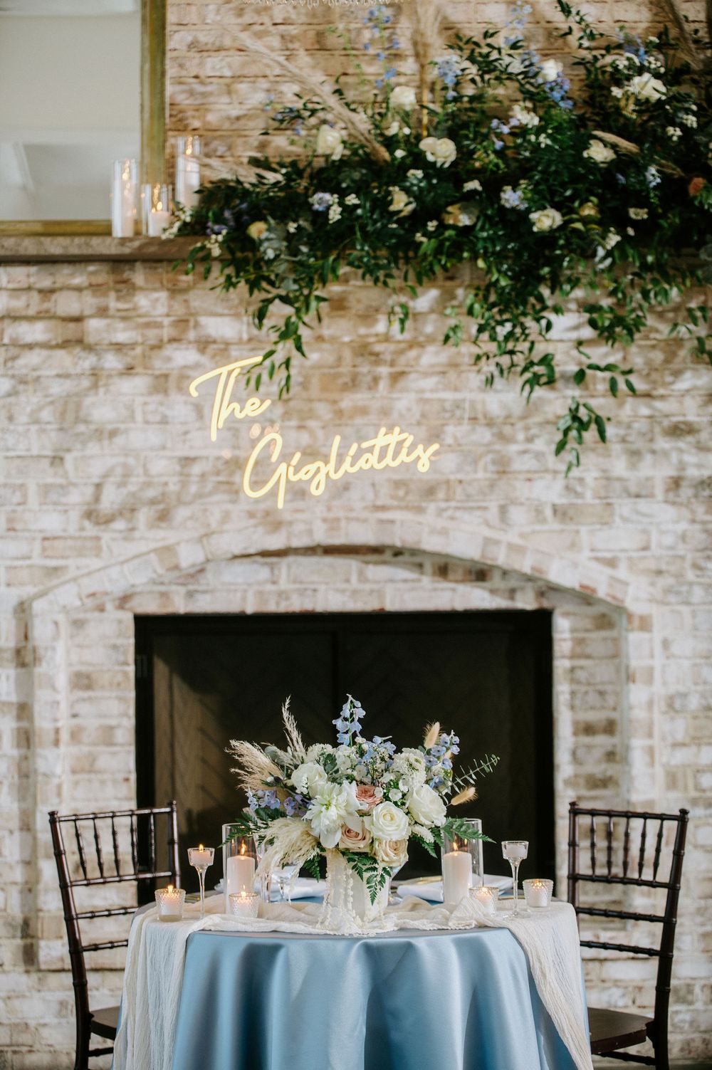 Elegant wedding reception tables with light blue linens, floral centerpieces and illuminated signage on exposed brick walls.