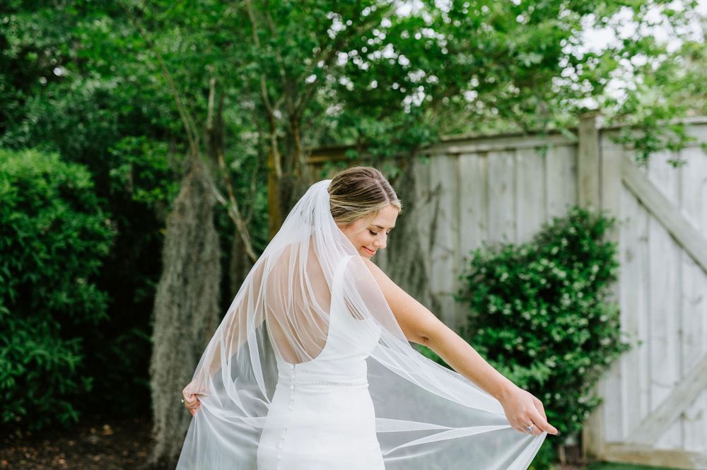 A bride in a flowing white veil poses in a lush garden setting during a summer wedding photoshoot.