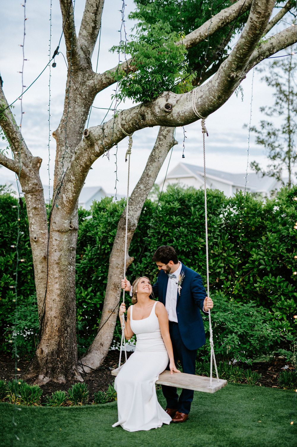 Couple shares romantic moment on tree swing in lush garden setting during outdoor wedding celebration.