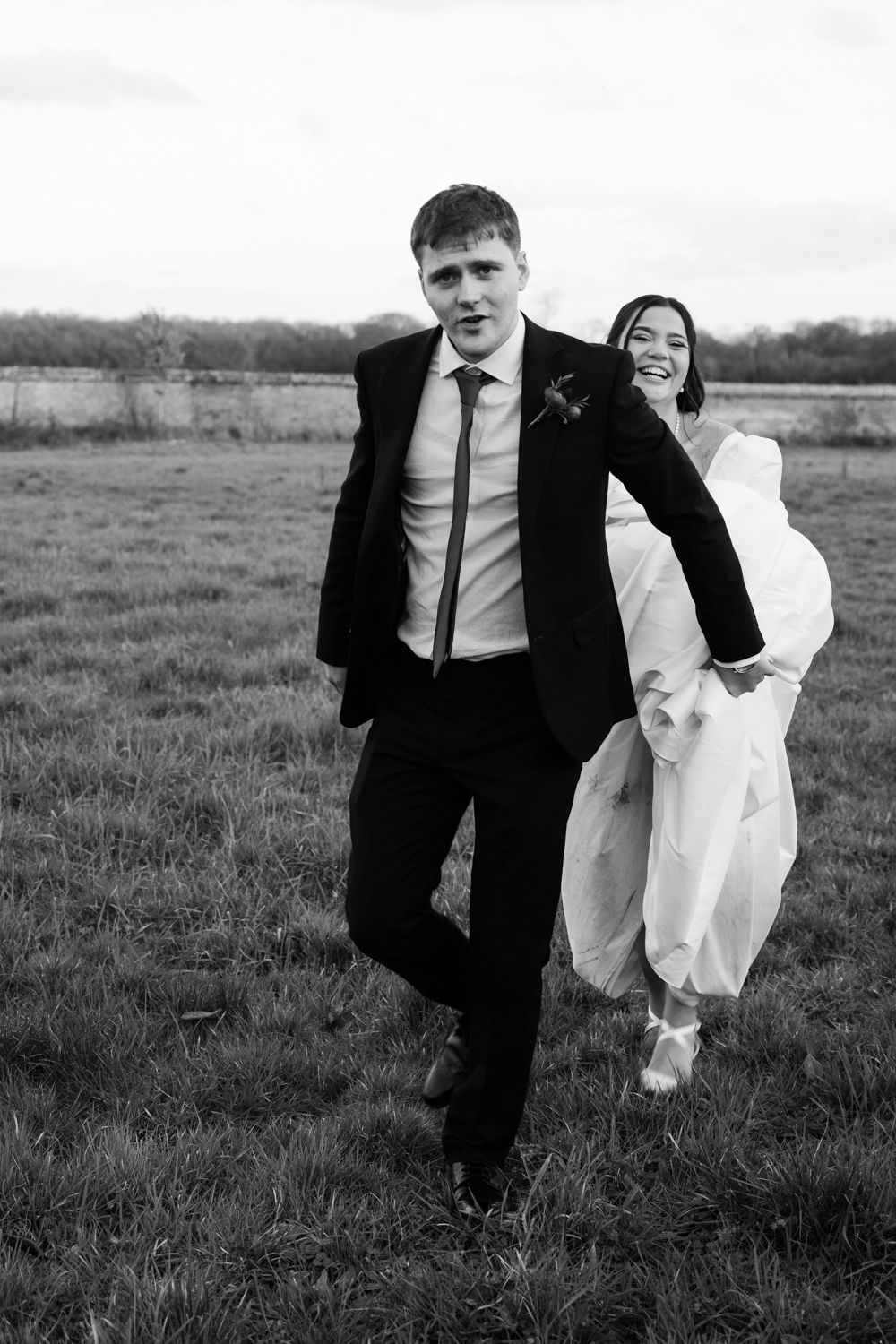 Black and white portrait of couple in formal attire standing together in grassy field.