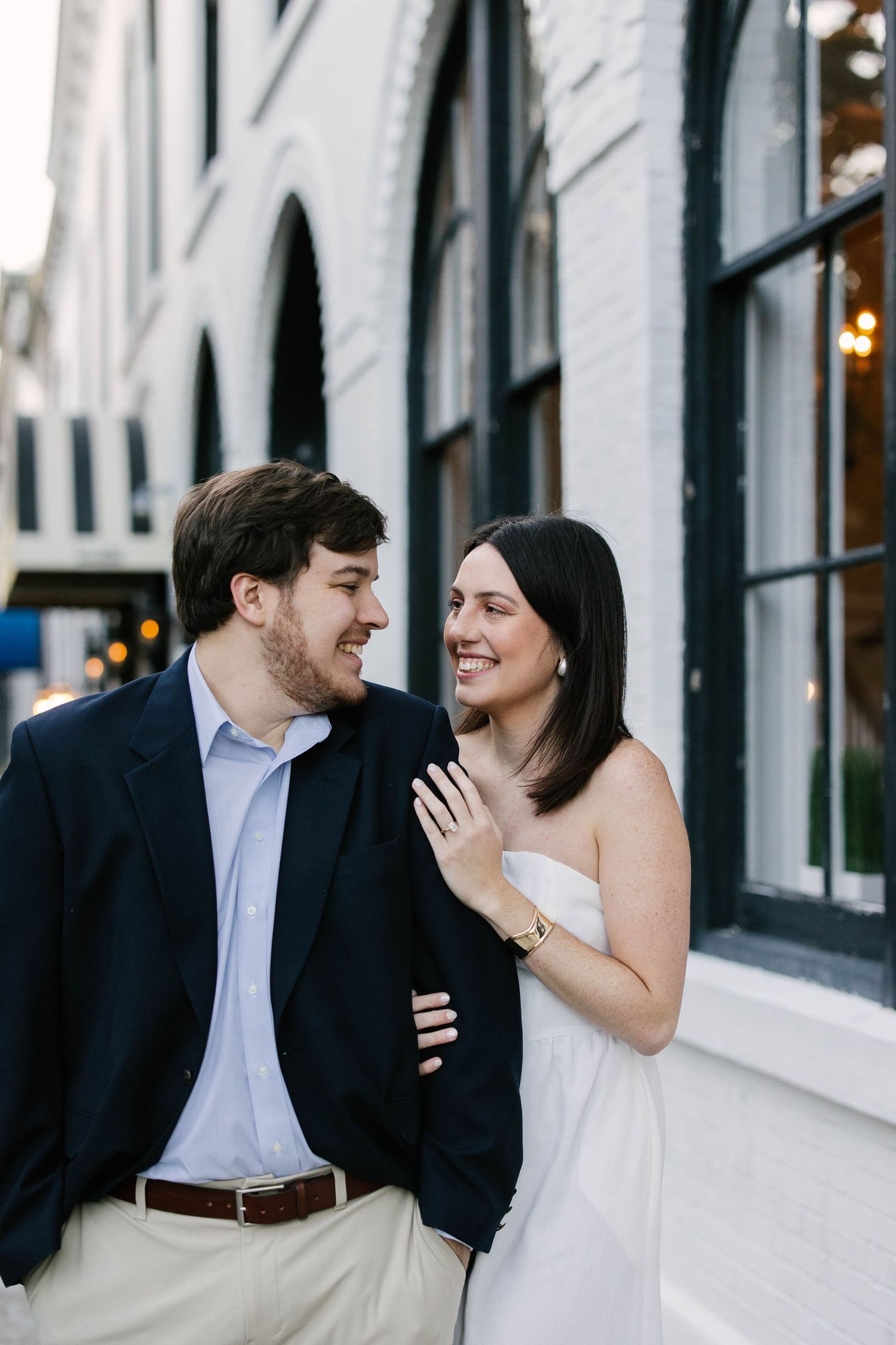 A couple shares a romantic moment together on a city street with white buildings in the background.