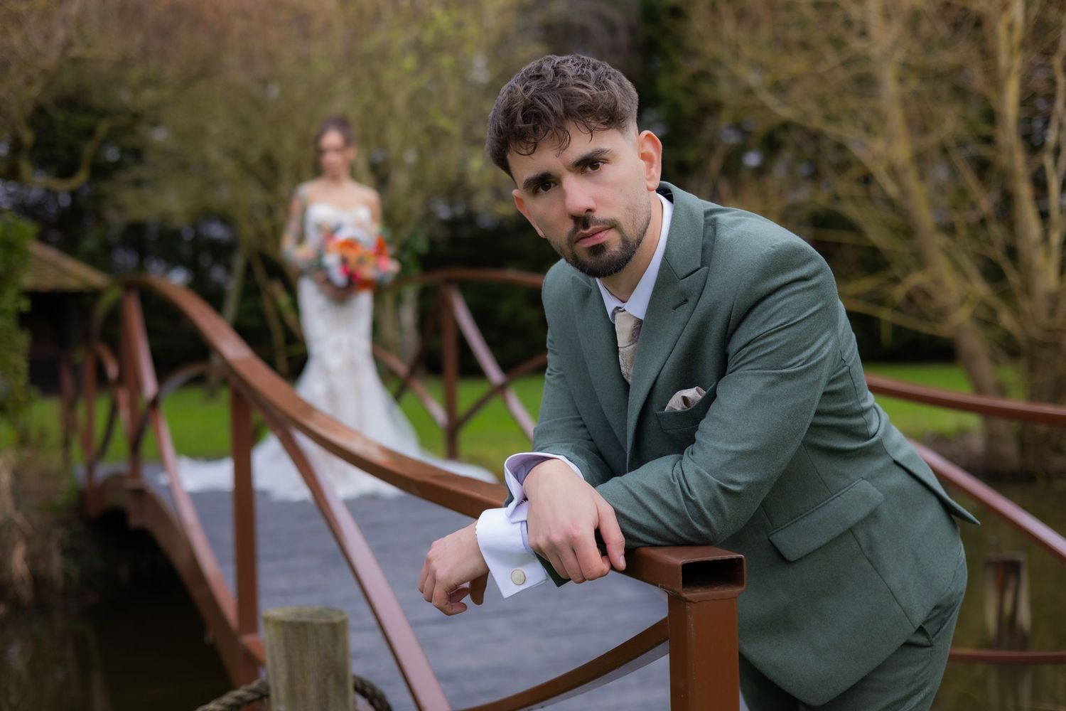 Wedding couple posing on rustic wooden bridge in garden setting.