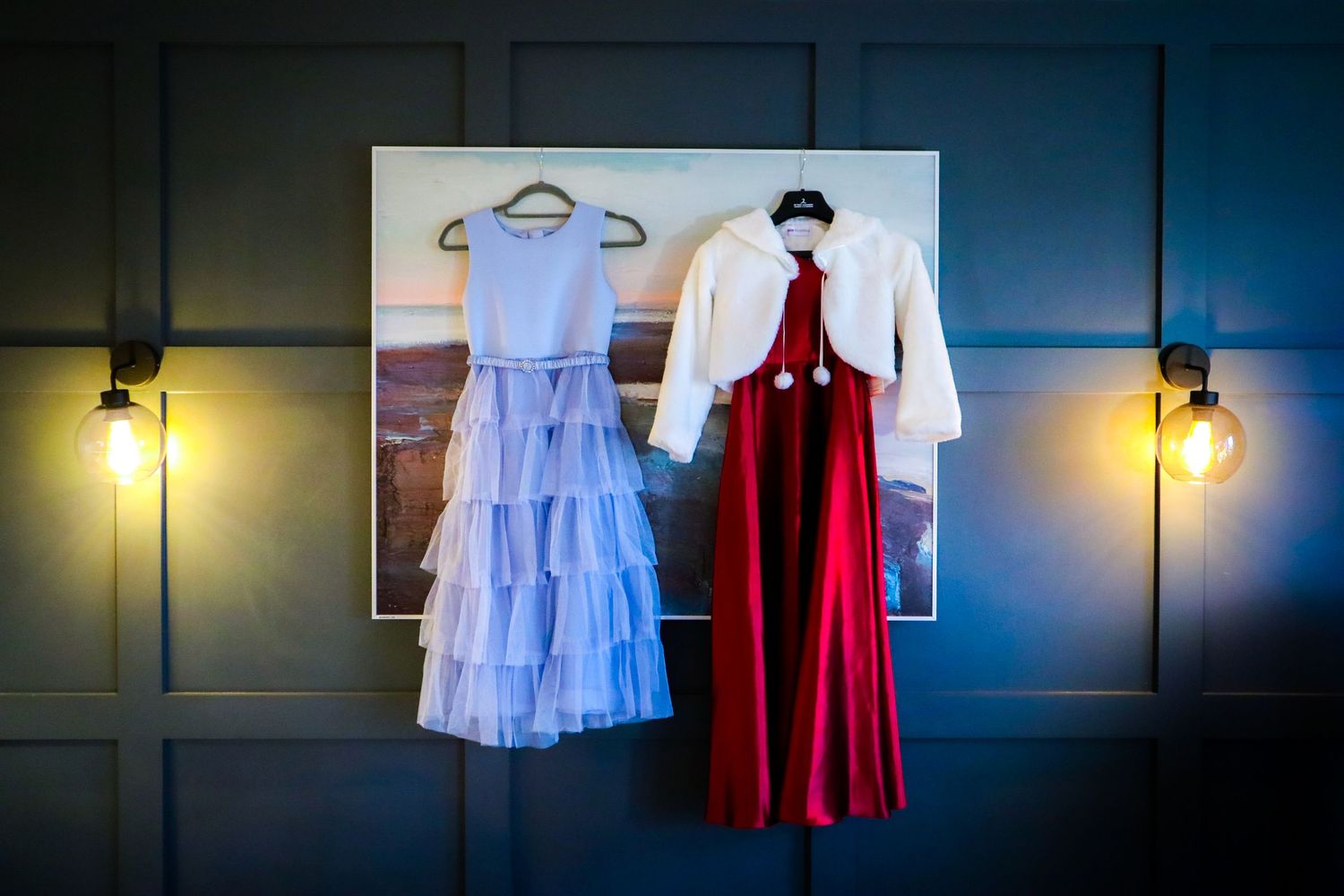Wedding dresses and formal attire displayed against a dark blue wall with dramatic lighting.