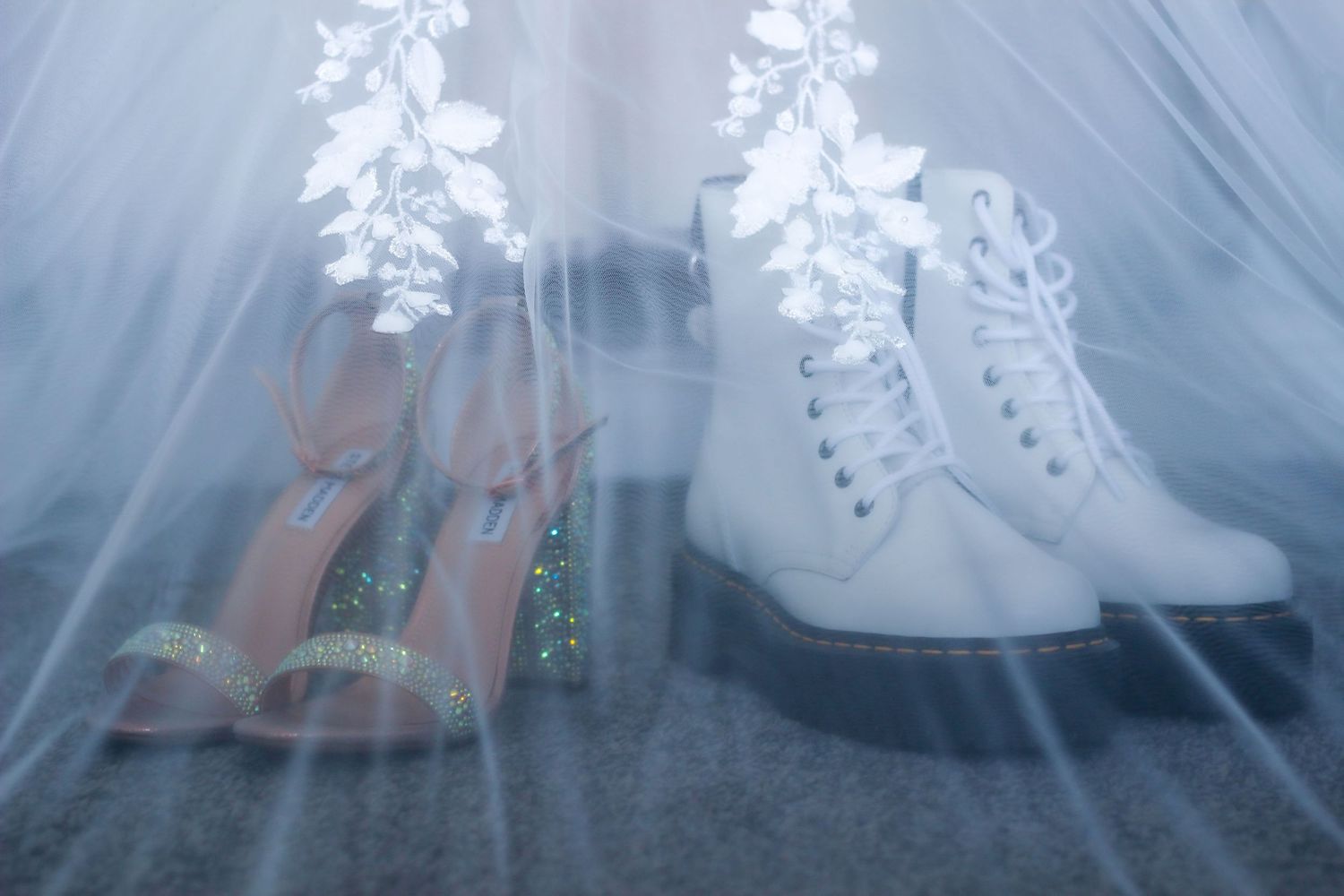Wedding shoes displayed under tulle - white boots and sparkly heels creating a romantic atmosphere.