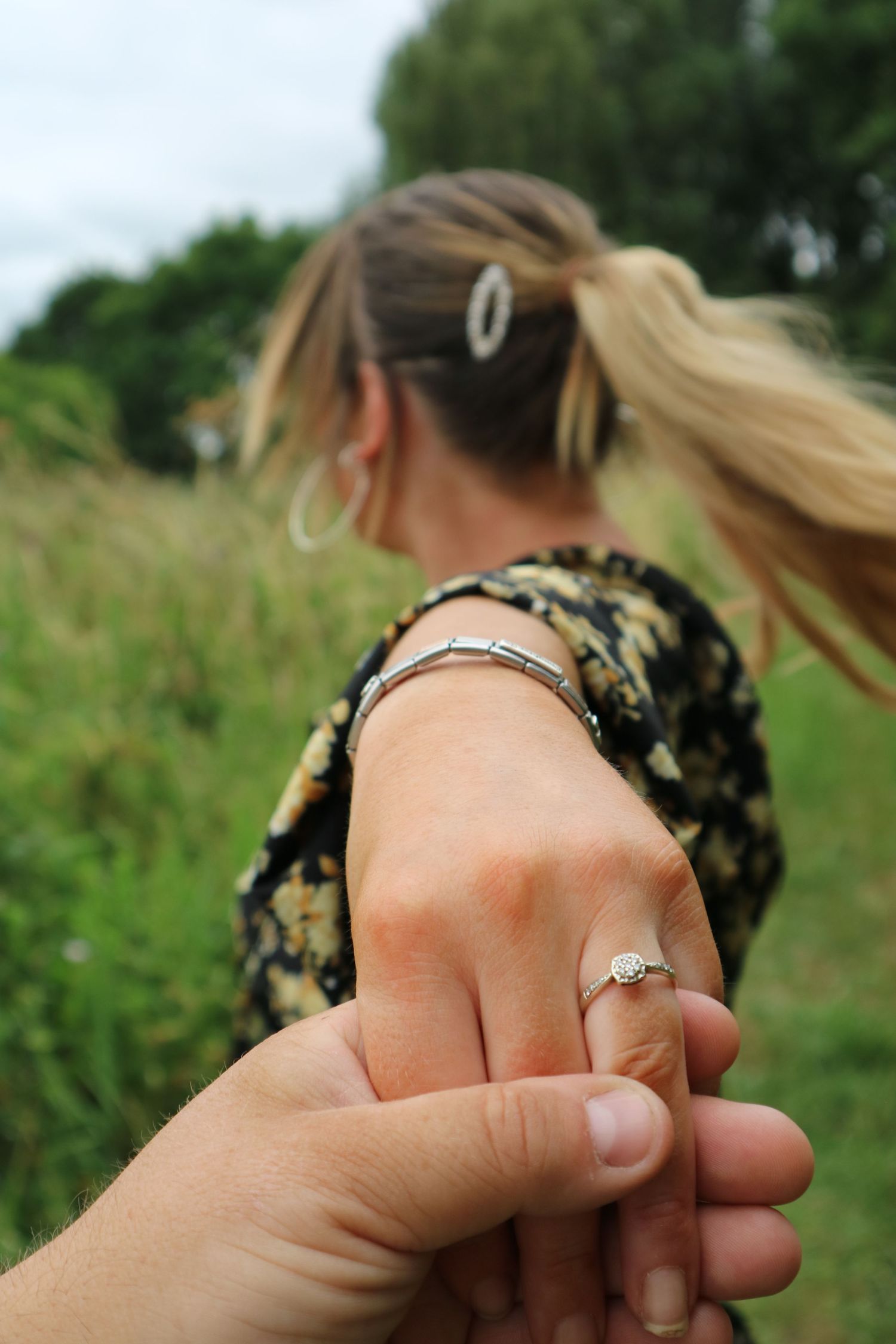 Close-up of engagement ring on hand with natural field backdrop.