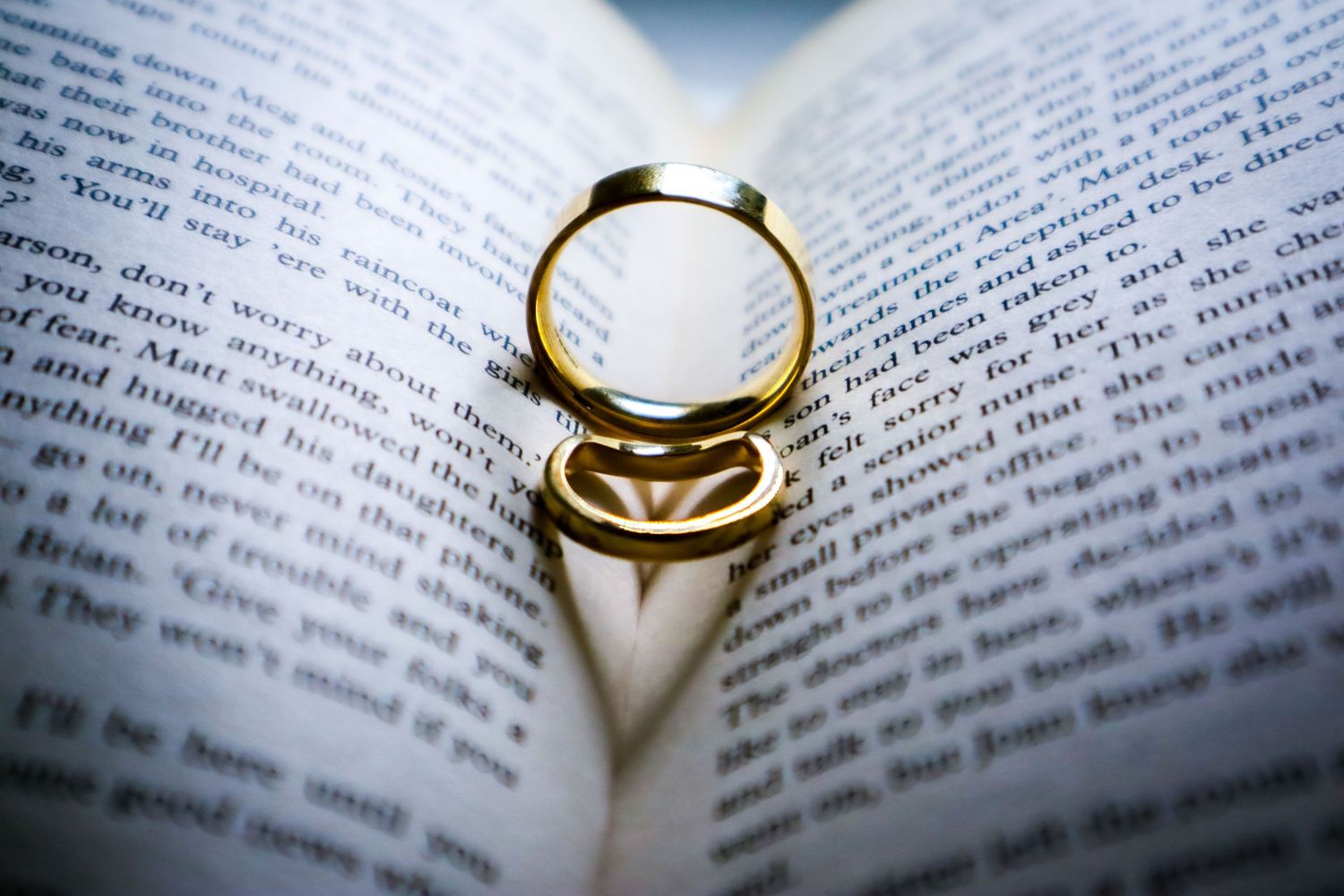 Wedding rings resting on open book pages with shallow depth of field.
