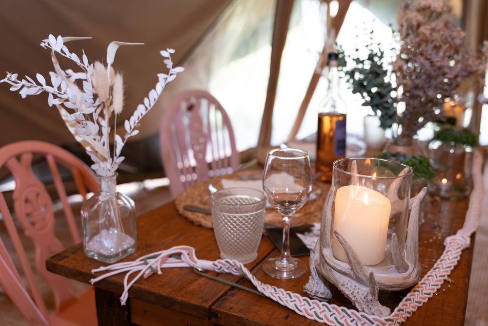 A cozy table setting with candlelight, wine glasses, and dried flowers on a rustic wooden dining table.