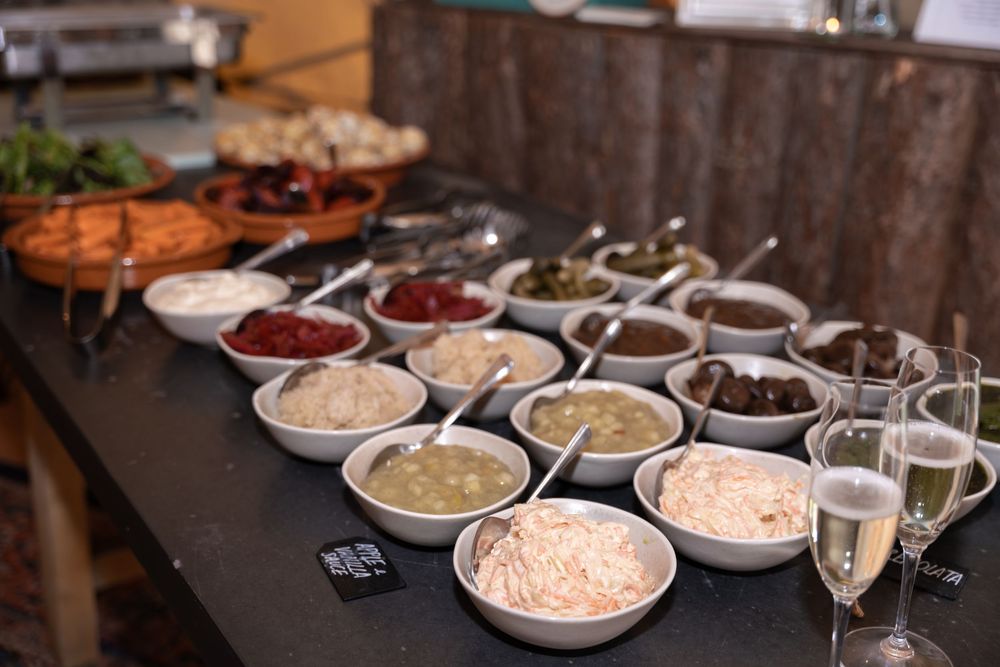 Assorted condiments and toppings in white bowls arranged on a rustic wooden table for a buffet-style meal service.