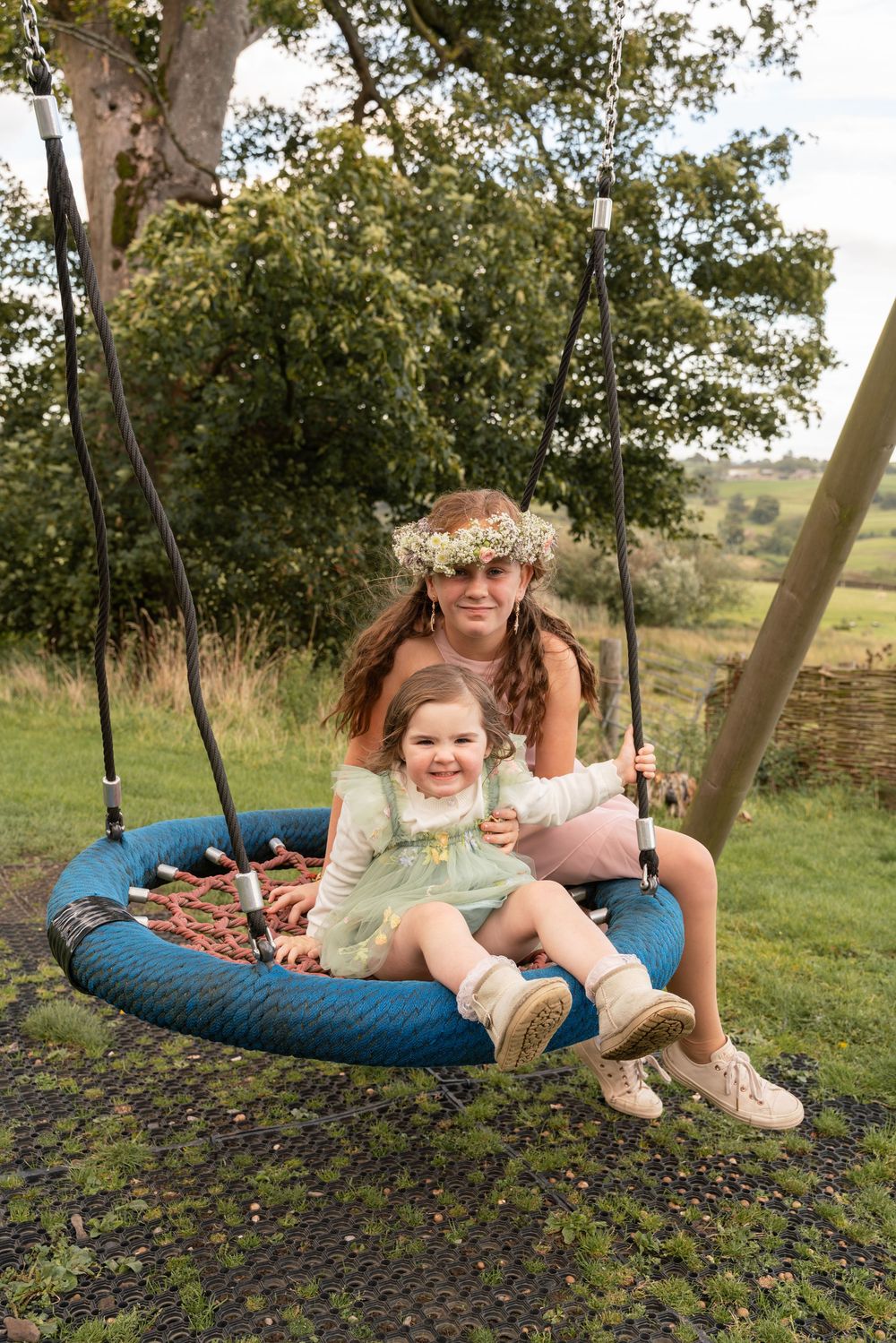 A round blue swing chair in a garden setting with floral decorations and natural surroundings.