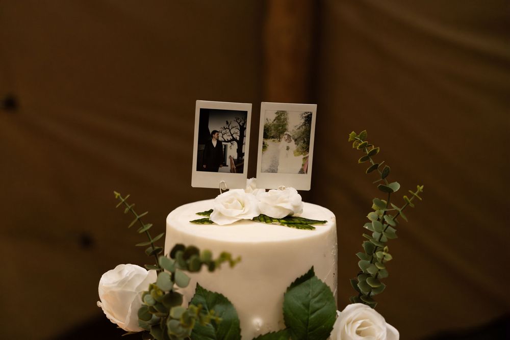 Wedding cake decorated with white flowers and greenery sits elegantly on a rustic wooden stand.