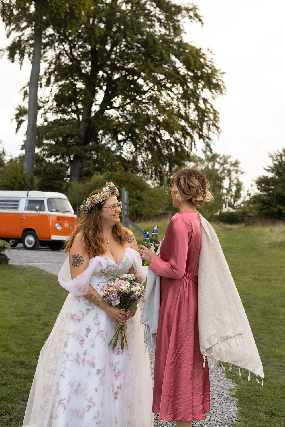 Wedding party in floral and pink dresses share joyful moments outdoors with vintage vehicles in background during a wedding in Lincolnshire.