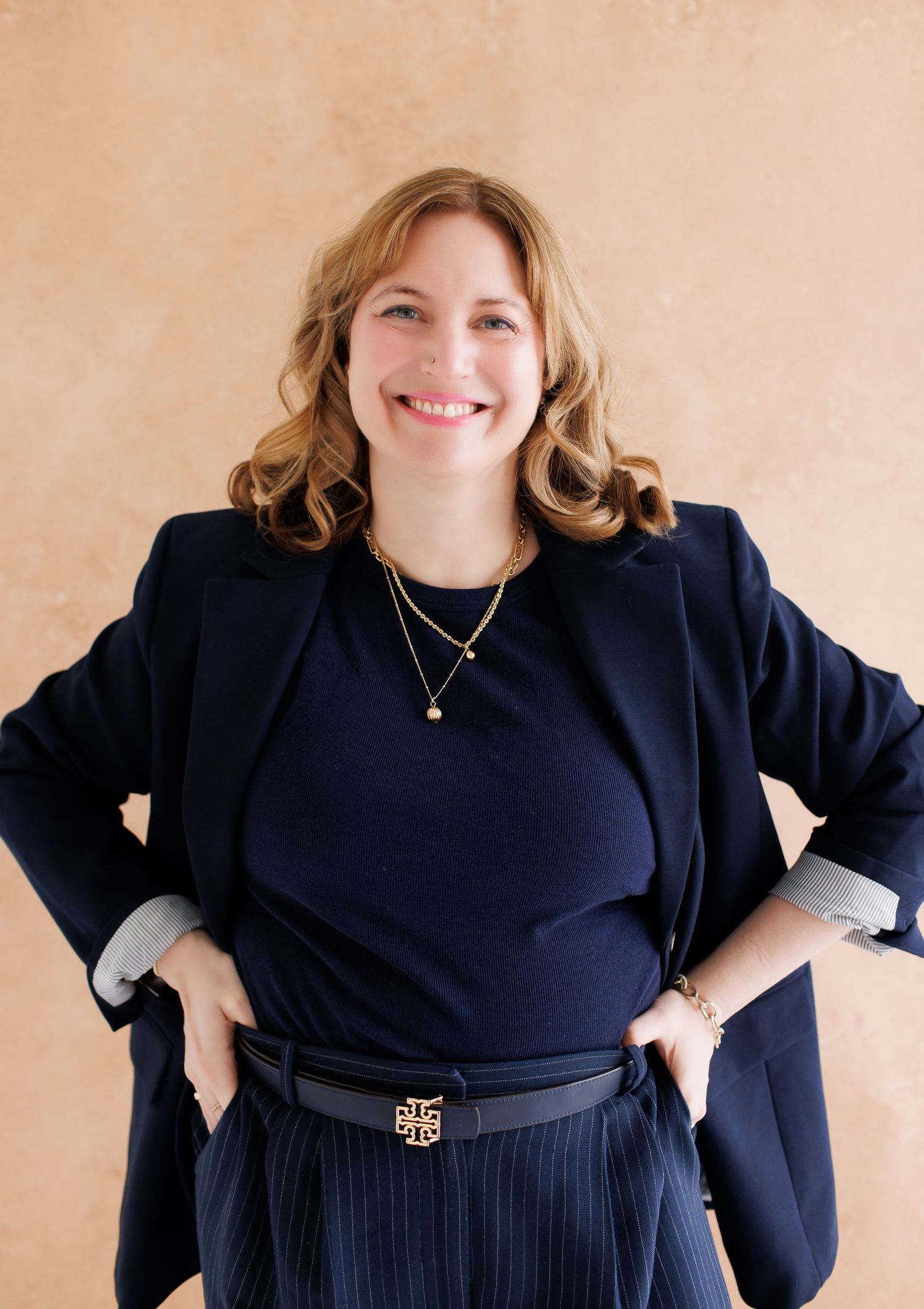 A person wearing a navy blue outfit poses with arms akimbo in a series of similar shots against a beige background.