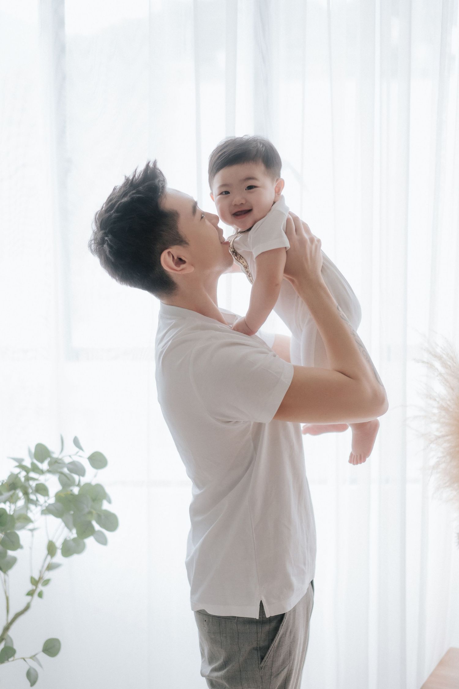 A family in white and olive outfits shares playful moments together in a bright minimalist setting.一家人穿著白色和橄欖綠服裝，在明亮簡約的環境中共享歡樂時光。
