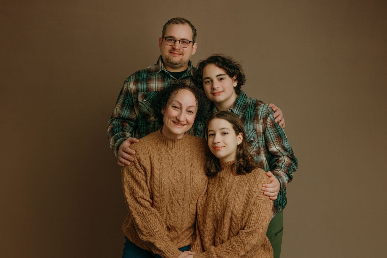 A photo of warm-toned family portraits showing people embracing and smiling against a brown background taken at the studio in Victoria BC.