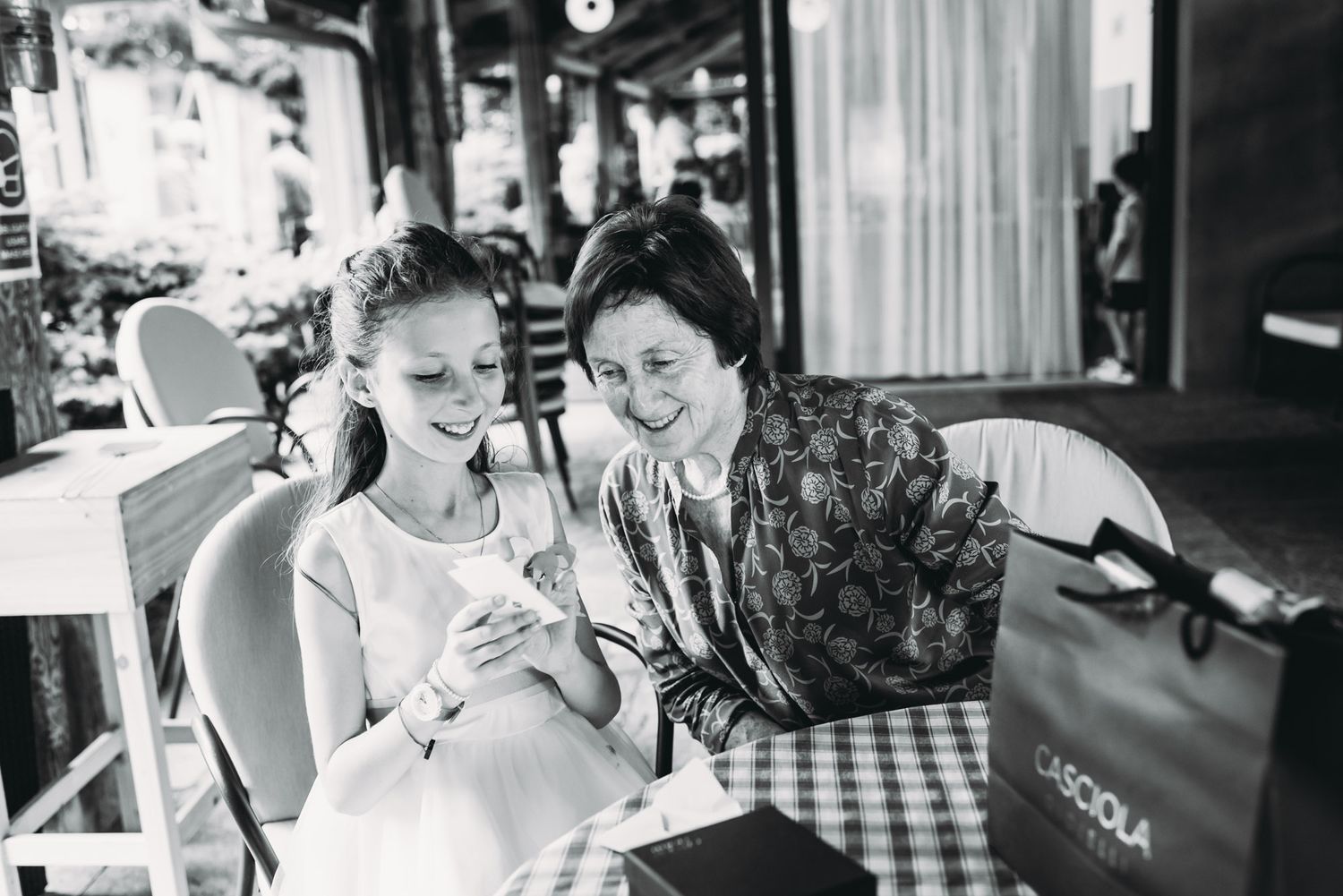A black and white candid photo of two people sharing a moment at an outdoor cafe.
