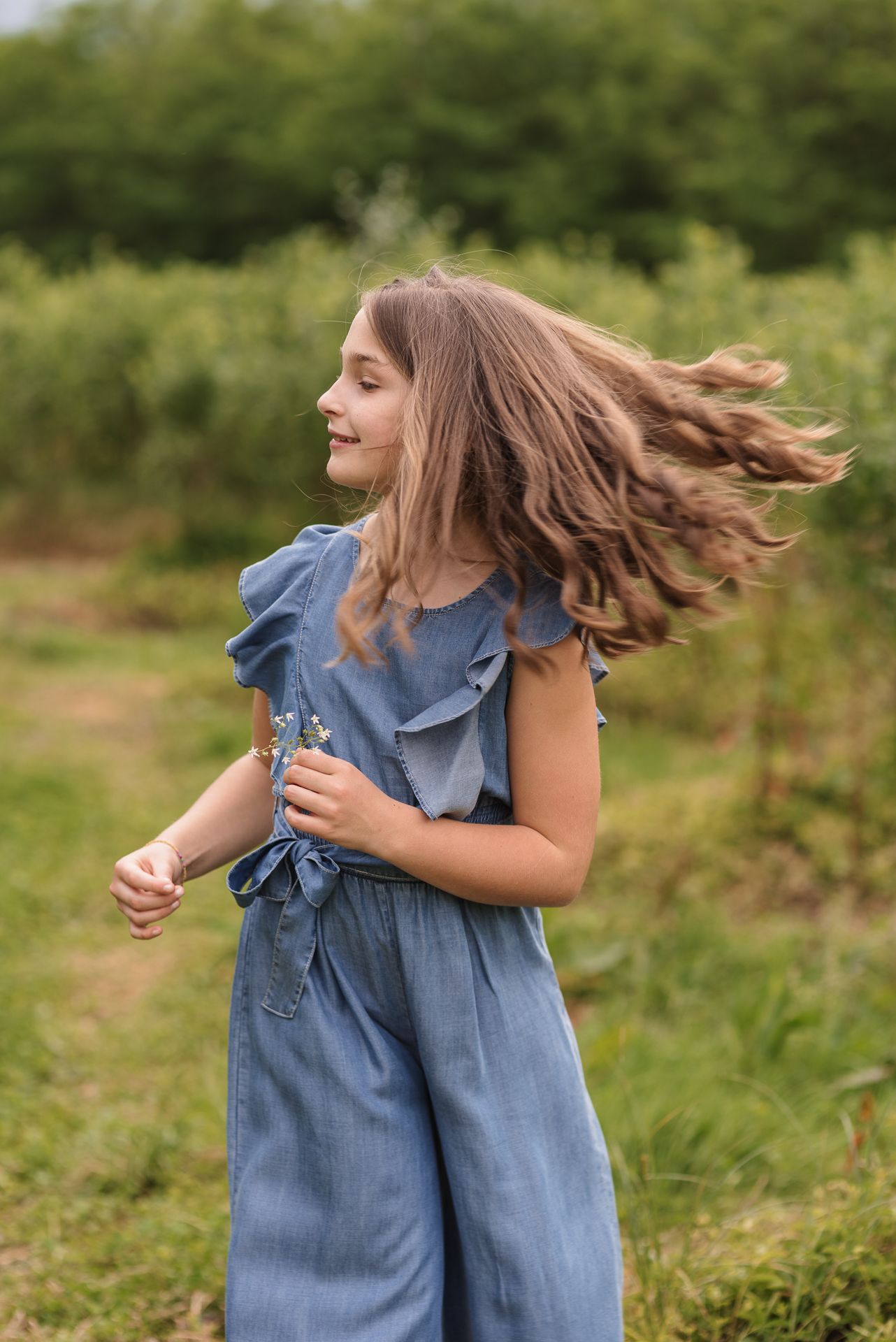 Young person dancing joyfully in a blue denim dress with ruffled sleeves in a sunny meadow.