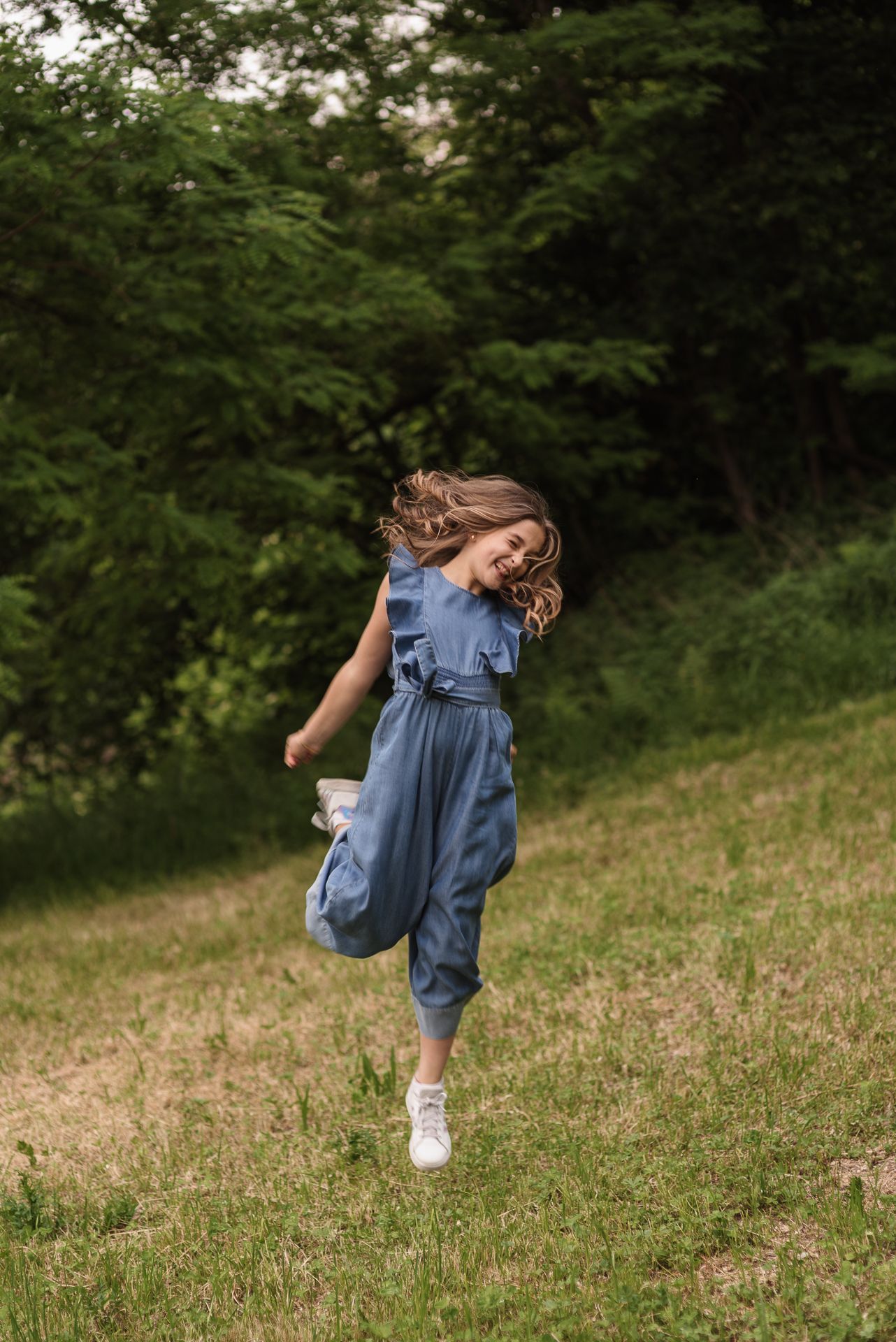 Person in blue jumpsuit twirling and dancing freely in a green summer field.