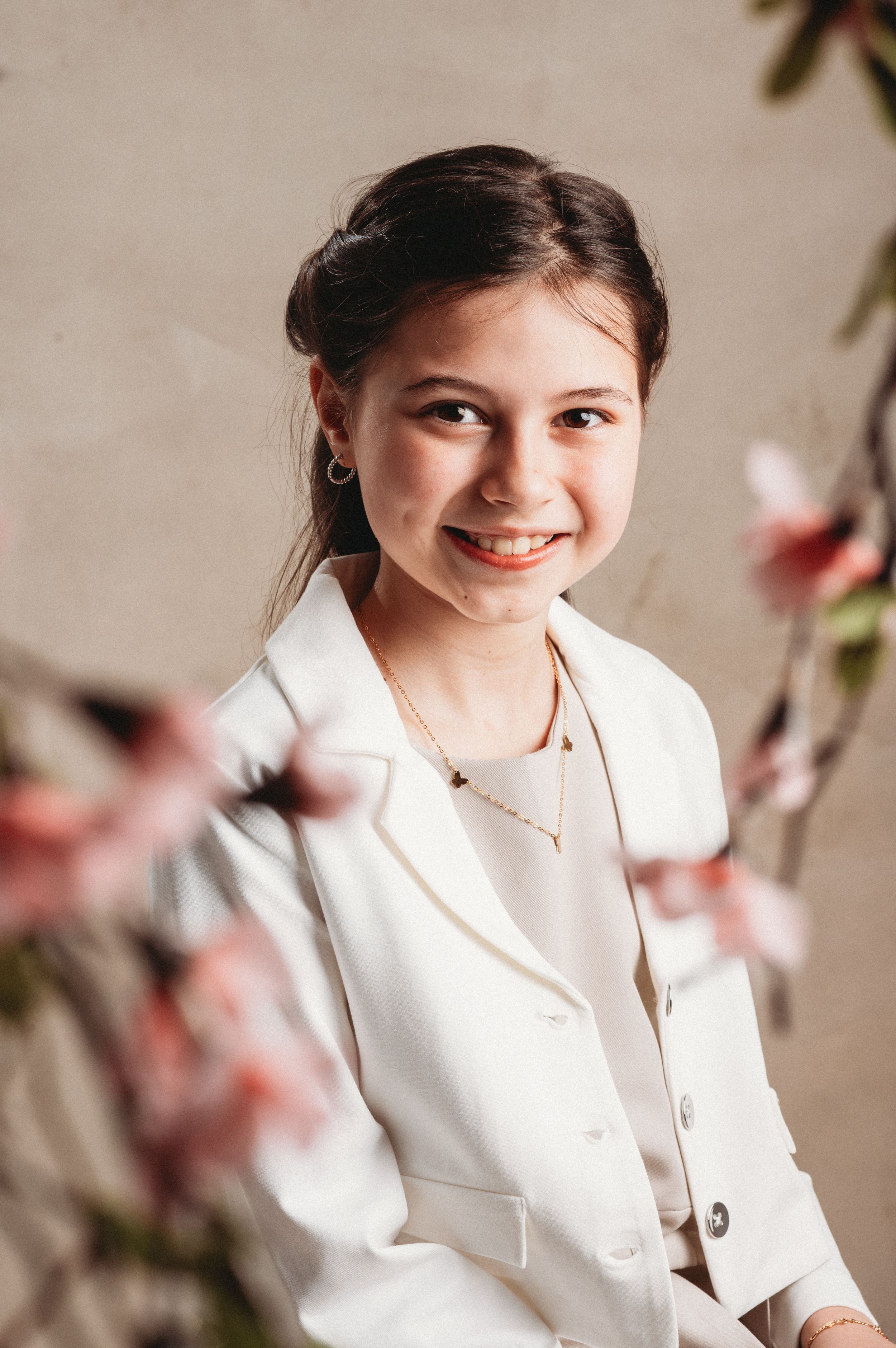 Portrait photo of someone in a crisp white blazer smiling warmly against a soft beige background with pink blossoms.