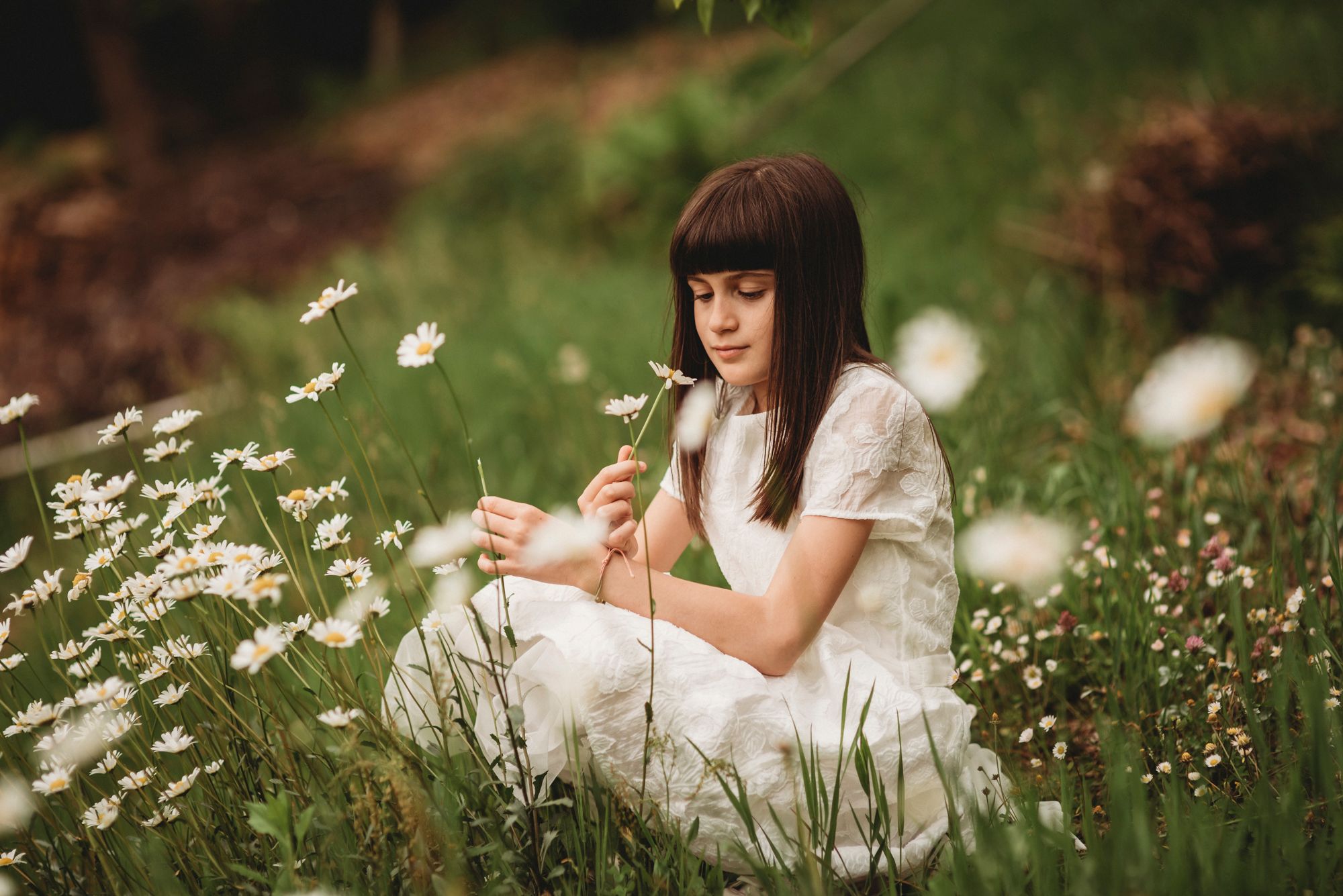 A person in a white dress sits among blooming daisies in a meadow.