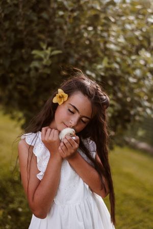Young person in white dress holding baby chicks outdoors in golden sunlight.