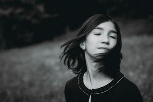 Artistic black and white portrait of person with windswept hair against dark background.