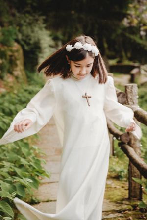 Person in white robe with floral headpiece twirling on garden path.