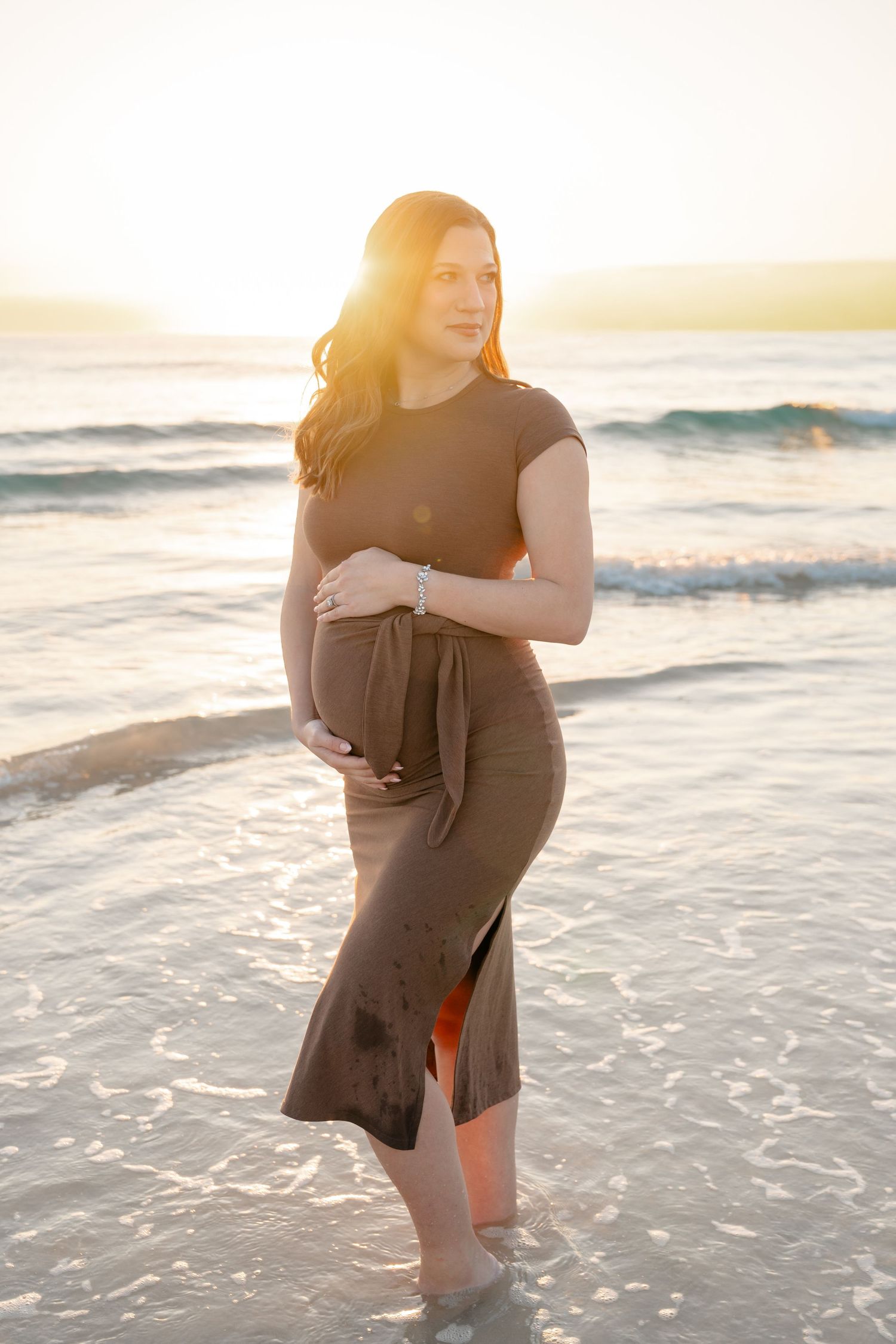 Couple embraces in shallow ocean waves during golden hour sunset at the beach.