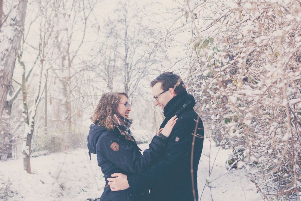 A couple embraces in a romantic winter scene surrounded by snow-covered trees and branches.