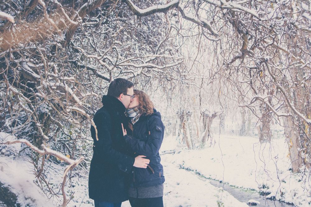 Two people share an intimate moment in a snowy winter wonderland surrounded by frost-covered trees.