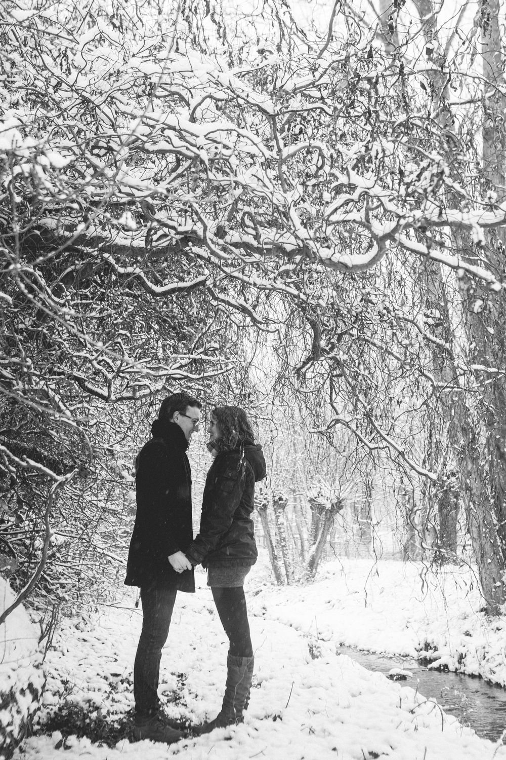 Two silhouettes share an intimate moment in a snow-covered forest with frost-covered branches overhead.
