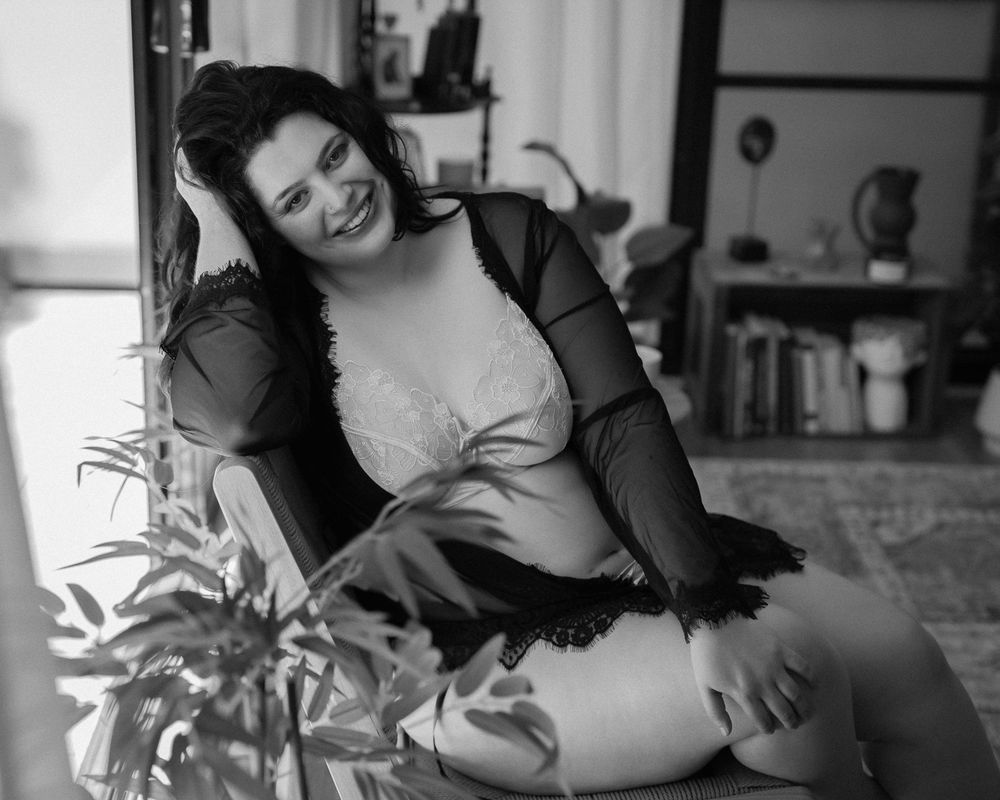 Vintage black and white photo of a person lounging on furniture with plants in the foreground.