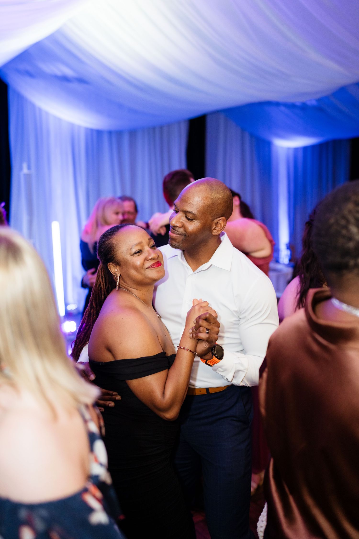 Couples dancing together at a wedding reception with blue uplighting and white drapes creating an elegant atmosphere.
