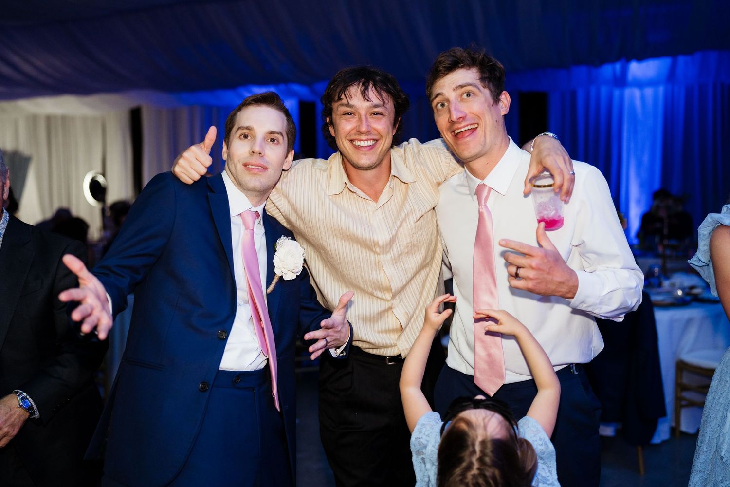 A group celebrates together at an event with blue lighting and white curtains in the background.